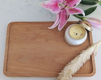 Può includere: Un vassoio di legno con una candela bianca in un barattolo di vetro con un coperchio dorato, un fiore secco e un giglio rosa.