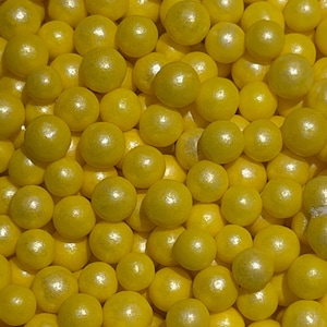 May include: A close-up shot of numerous yellow, spherical candies. The candies have a slightly pearlescent sheen, and they are densely packed together, filling the frame. The overall effect is a vibrant, textured display of confectionery.