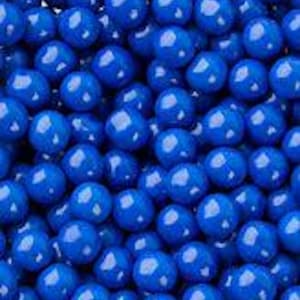 May include: A close-up shot of numerous small, round, blue candies. The candies are uniformly colored and have a glossy finish, filling the frame. The overall impression is of a dense, textured field of vibrant blue spheres.