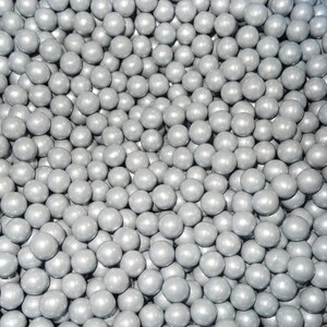 May include: A close-up shot of a large pile of small, round, silver-colored spheres. The spheres are densely packed together, creating a textured surface. The lighting highlights the glossy finish of each sphere, giving them a reflective quality.