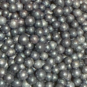 May include: Close-up of a pile of small, dark gray spheres. The spheres have a metallic sheen and vary slightly in size. The image is tightly framed, filling the view with the textured surface of the spheres.