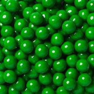 May include: A close-up shot of a pile of bright green, round candies. The candies have a glossy finish and are densely packed together, filling the frame. The uniform color and shape create a visually appealing texture.