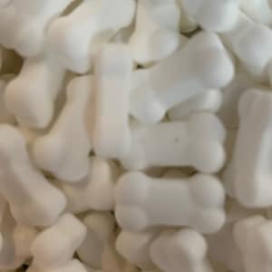 May include: A close-up shot of numerous white, bone-shaped sweets. The candies are smooth and rounded, mimicking the appearance of small dog bones. The lighting is good, emphasizing the texture and shape of the treats.