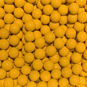 May include: A close-up shot of numerous yellow, spherical objects. The spheres are evenly distributed, filling the frame. The objects have a smooth, glossy texture and a consistent, bright yellow color, creating a visually uniform pattern.