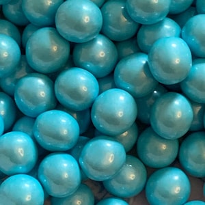 May include: A close-up shot of numerous, round, light blue candies with a glossy, pearl-like finish. The candies are tightly packed together, filling the frame. The color is a vibrant, eye-catching shade of turquoise.