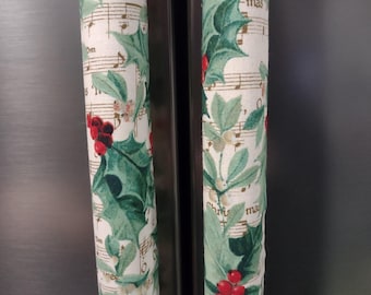 May include: Two cylindrical fabric covers with a Christmas theme. The covers have a white background with green holly leaves, red berries, and musical notes. The text "st-mas" is visible on the fabric.