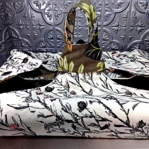 May include: A fabric bag with a single handle featuring a cream-colored exterior with a black botanical print of wildflowers and small pink accents. The interior lining is a solid brown fabric with a green and brown leaf pattern on the handle.