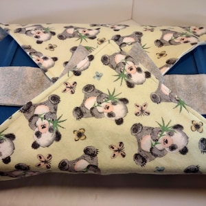 May include: A blue container covered with a light yellow fabric featuring a panda bear pattern. The pandas are grey and white, holding bamboo. Butterflies and flowers are also printed on the fabric. A grey strap is attached to the container.