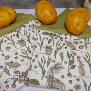 Può includere: Tre patate dorate poggiano su due strofinacci da cucina. Gli strofinacci presentano un design stravagante di topi, fragole e fiori. Gli strofinacci sono piegati con un bordo verde.