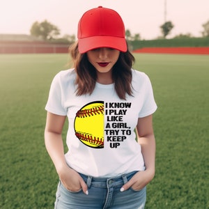 May include: White t-shirt with a softball graphic and the text "I know I play like a girl, try to keep up".