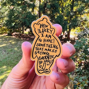 May include: A tan sticker in the shape of a bear with the text "How lucky I am to have something that makes saying goodbye so hard." The sticker also includes the words "Winnie the Pooh."
