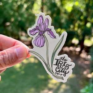 May include: A sticker featuring a purple iris flower with green leaves and the text "the Iris City" with the words "griffith, ga" underneath.