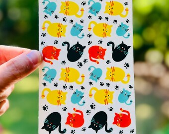 May include: A sheet of colorful cat stickers with paw prints. The cats are yellow, blue, red, and black.