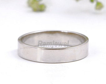 Puede incluir: Un anillo de banda plano de color plateado. El anillo tiene un diseño simple y minimalista con una superficie lisa y pulida. El anillo probablemente está hecho de un metal precioso, como plata o platino. Una joya clásica.