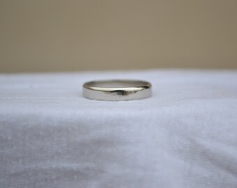 Puede incluir: Un anillo de banda de metal plateado pulido con una superficie lisa y plana y un perfil redondeado. El anillo presenta un acabado reflectante de alto brillo que capta la luz, mostrando un diseño circular simple y continuo sin grabados.