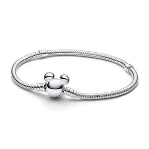 Puede incluir: Una pulsera plateada con un dije en forma de Mickey Mouse. La pulsera tiene un dise&ntilde;o de cadena de serpiente y un cierre. El dije tiene forma redondeada con dos peque&ntilde;os c&iacute;rculos en la parte superior, que se asemejan a las orejas de Mickey Mouse.