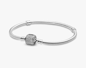 May include: A silver bracelet with a round, textured clasp encrusted with small, sparkling stones. The bracelet's band is a flexible, twisted design. The clasp is centered on the bracelet, which is displayed against a plain white background.