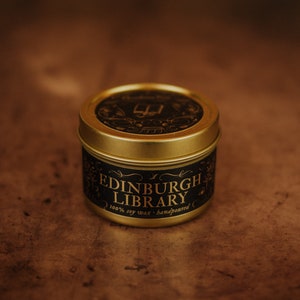 Front shot of Edinburgh Library 3.3 oz soy candle in a gold tin with top and black and gold foil labels with vintage illustrations on the front and lid