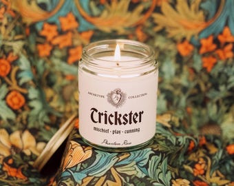 May include: A lit glass jar candle labelled "Trickster" with the words "mischief - play - cunning" below. The candle is part of the "Archetype Collection" and has a "Phantom Rose" scent. The background features a floral pattern.