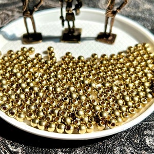May include: A white plate filled with gold-colored beads, surrounded by three small gold-colored figurines. The figurines are of people carrying jugs on their heads.