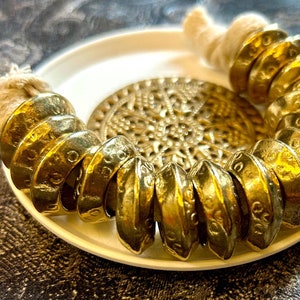 Puede incluir: Un brazalete de metal dorado hecho de múltiples anillos apilados. El brazalete está en un plato blanco con un diseño decorativo.