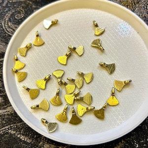 Peut inclure: Plusieurs petits breloques en métal doré en forme de hachettes, disposées sur une assiette blanche texturée. Les breloques ont un design détaillé et une boucle pour les bijoux ou l'artisanat. Fond sombre et texturé.