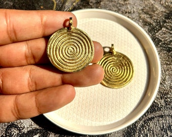 May include: Two gold-colored metal pendants with a spiral design. The pendants are round and have a hole at the top for hanging.