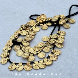 Puede incluir: Un collar de oro con múltiples hileras de pequeñas cuentas redondas en forma de espiral. Las cuentas están enhebradas en un cordón negro.