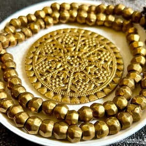 May include: A gold necklace with a large, ornate, circular pendant. The necklace is made of small, faceted beads.
