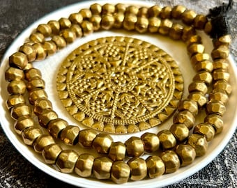 Op de afbeelding: Een gouden ketting met een grote, sierlijke, ronde hanger. De ketting is gemaakt van kleine, gefacetteerde kralen.