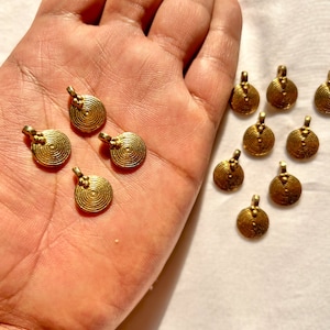 Peut inclure: Un ensemble de 12 breloques en métal doré avec un design circulaire. Chaque breloque présente un motif de cercles concentriques et une petite perle en haut.