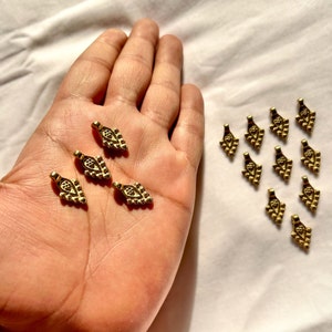 May include: A collection of 15 gold-toned metal charms in the shape of a stylized leaf. The charms have a detailed design with small beads around the edges and a central design.
