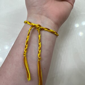 May include: A yellow and brown braided friendship bracelet with tassels.