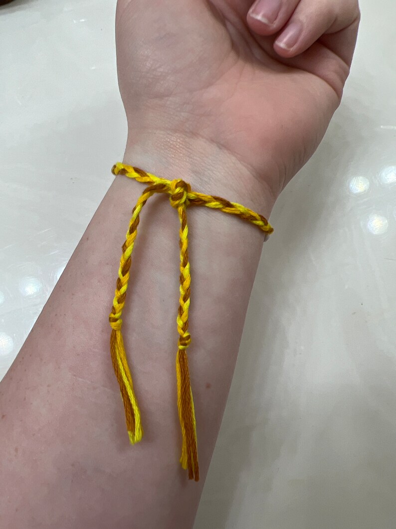 May include: A yellow and brown braided friendship bracelet with tassels.