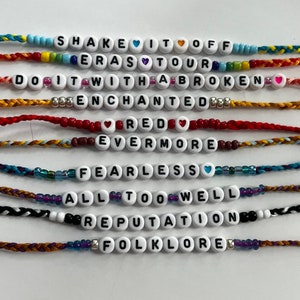 May include: Ten colorful friendship bracelets with different Taylor Swift album titles spelled out in white beads. The bracelets are made with colorful embroidery floss.