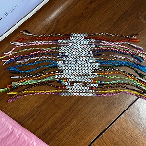 May include: A collection of 20 colorful friendship bracelets with beaded words, including "Maroon", "Red", "Lavender Haze", "Lover", "Shake It Off", "Paper Rings", "Midnights", "Speak Now", "Get Away Car", "Stay Beautiful", "On Your Own Kid", "Wildest Dreams", "Reputation", "Love Story", "Taylor Swift", "Eras Tour", "All Too Well", "Evermore", "Fearless", "Cruel Summer".