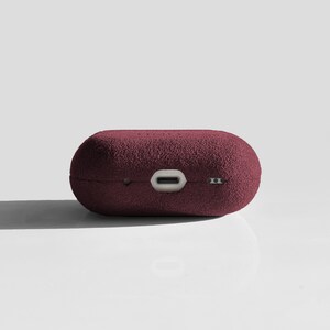 Puede incluir: Una funda de felpa color burdeos para auriculares inal&aacute;mbricos. La funda tiene una superficie texturizada y un puerto de carga.