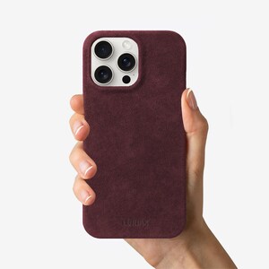 May include: A burgundy suede phone case with a white camera bump and the word "LURVEY" embossed on the bottom.
