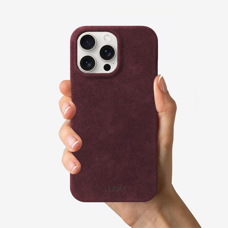 May include: A burgundy suede phone case with a white camera bump and the word "LURVEY" embossed on the bottom.