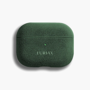 Puede incluir: Una funda verde oscuro texturizada para auriculares inalámbricos. La funda tiene forma rectangular redondeada con una pequeña luz verde y la palabra "IURIAX" impresa en la parte delantera. La funda está diseñada para proteger y guardar los auriculares.