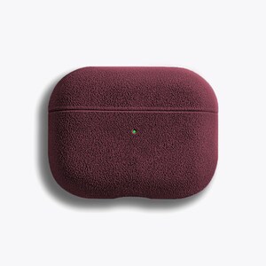 Puede incluir: Una funda de silicona de color rojo burdeos para AirPods Pro con un acabado texturizado y peludo.