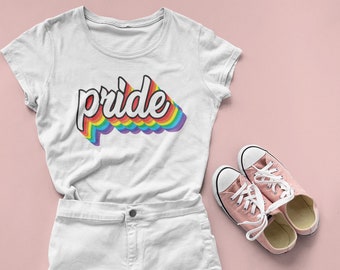 Può includere: Maglietta bianca con una grafica arcobaleno che dice "pride". La maglietta è abbinata a pantaloncini di jeans bianchi e scarpe da ginnastica rosa.