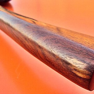 May include: Close-up of a dark brown wooden handle with a smooth, polished finish. The handle has a slightly rounded shape and a natural wood grain pattern.