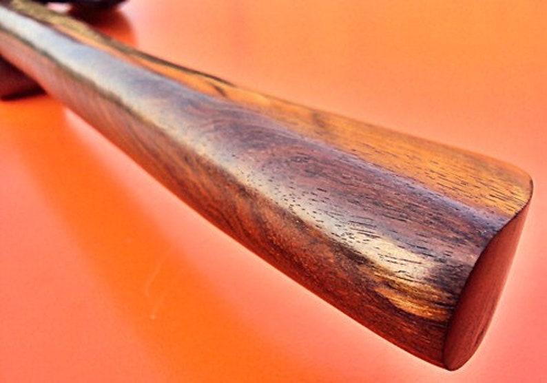 May include: Close-up of a dark brown wooden handle with a smooth, polished finish. The handle has a slightly rounded shape and a natural wood grain pattern.