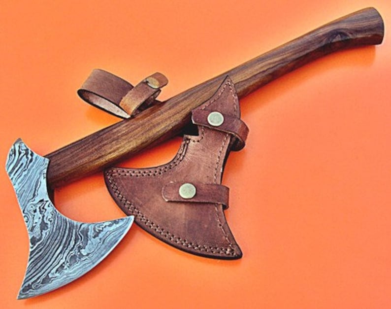 May include: A hand-forged Damascus steel axe with a wooden handle and a brown leather sheath. The axe has a unique, swirling pattern on the blade.