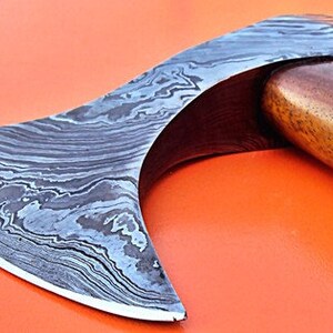 May include: A hand-forged axe with a curved blade and a wooden handle. The blade is made of Damascus steel and has a distinctive pattern.