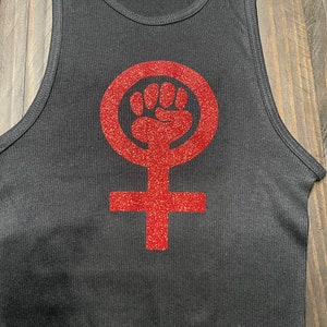 K&ouml;nnte beinhalten: Schwarzes Tanktop mit einem roten Glitzer-Feministensymbol mit einer erhobenen Faust.