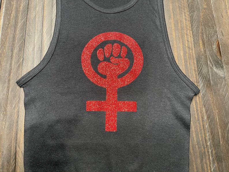 K&ouml;nnte beinhalten: Schwarzes Tanktop mit einem roten Glitzer-Feministensymbol mit einer erhobenen Faust.