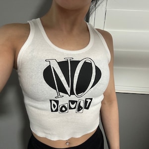 Op de afbeelding: Wit getailleerd tanktop met zwarte tekst die "NO DOUBT" luidt in een gestileerd lettertype.