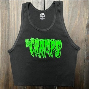 Pu&ograve; includere: Canotta nera a coste con la scritta verde neon "THE CRAMPS" sul davanti. La canotta ha uno scollo tondo ed &egrave; senza maniche. L'immagine &egrave; di una canotta corta, probabilmente per un abbigliamento casual.
